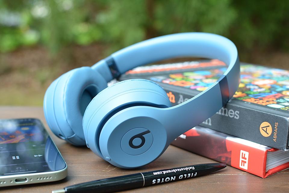 <p>Beats Solo 4 laying on two books with an iPhone to the left and a black pen in the foreground.</p>
