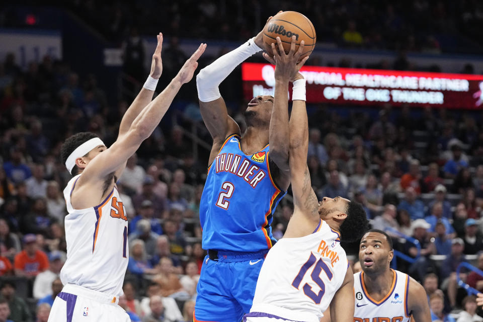 Oklahoma City Thunder guard Shai Gilgeous-Alexander (2) shoots between Phoenix Suns guard Devin Booker, left, and guard Cameron Payne (15) in the first half of an NBA basketball game Sunday, April 2, 2023, in Oklahoma City. (AP Photo/Sue Ogrocki)
