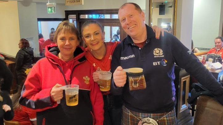 Francesca stands in the middle of her mum and dad in a pub. They are all smiling and looking happy and are holding pints of beer.