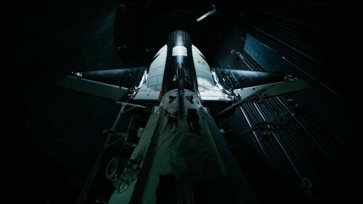  Close up view, from behind, of a black and white space plane in a dark room. 