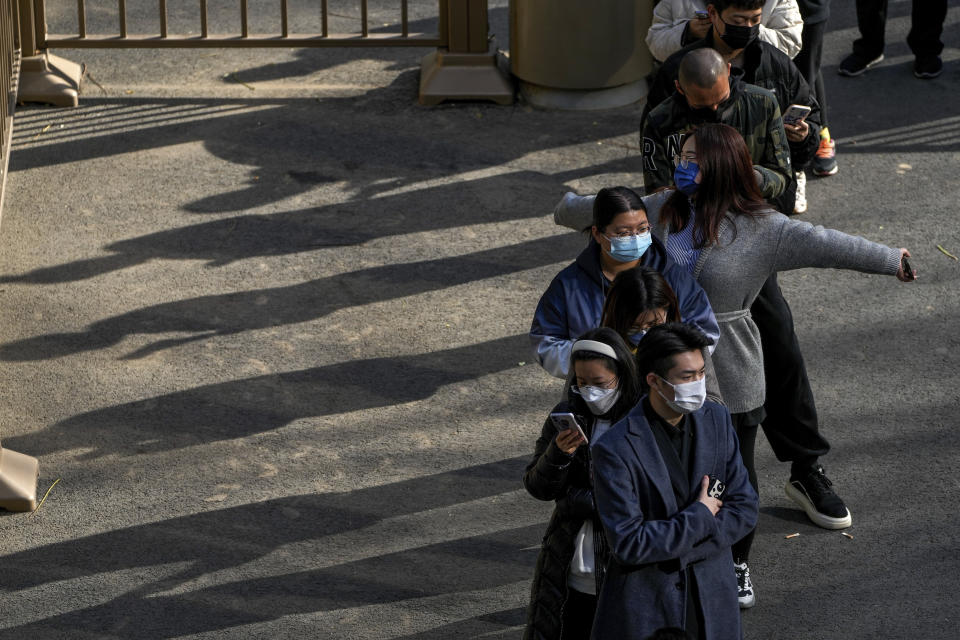 A woman wearing a face mask stretches her arms as she and masked residents wait in line for their routine COVID-19 tests at a coronavirus testing site in Beijing, Wednesday, Nov. 16, 2022. Chinese authorities locked down a major university in Beijing on Wednesday after finding one COVID-19 case as they stick to a "zero-COVID" approach despite growing public discontent. (AP Photo/Andy Wong)