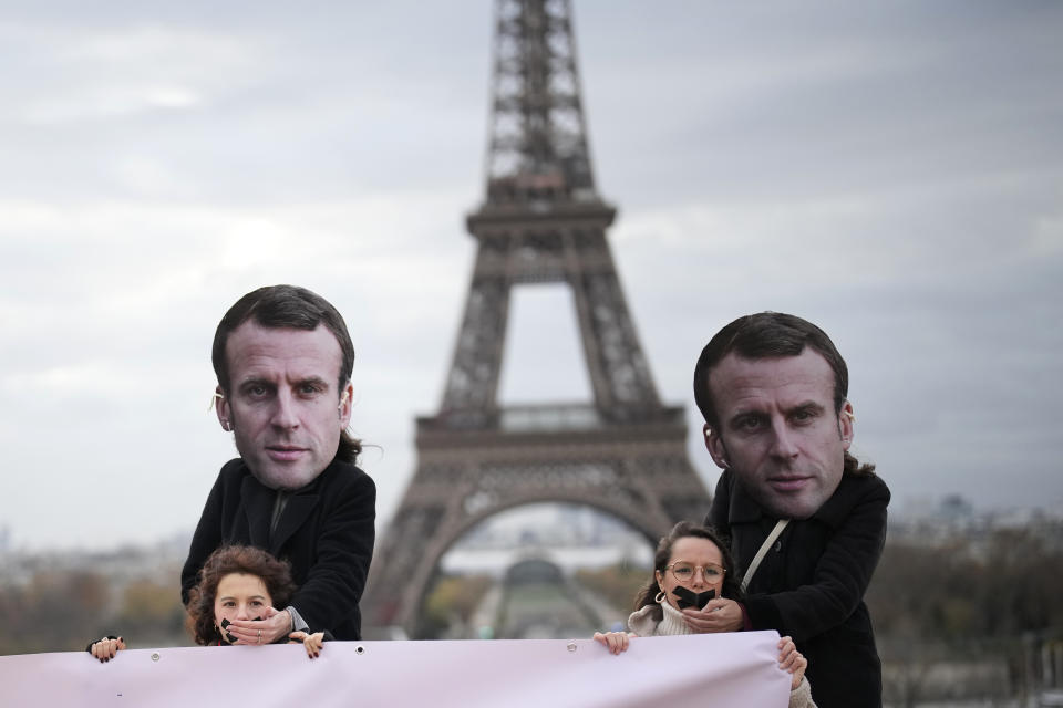 Gagged activists hold a placard as persons wearing a mask of French President Emmanuel Macron stand behind putting his hand on their mouth during a protest Friday, Nov. 24, 2023 in Paris. Activists say that France is vetoing a European decision on rape definition based on lack of consent. The large majority of EU member countries already treat violence against women and girls as a crime but the Commission said last year there are gaps in national legislation. (AP Photo/Christophe Ena)