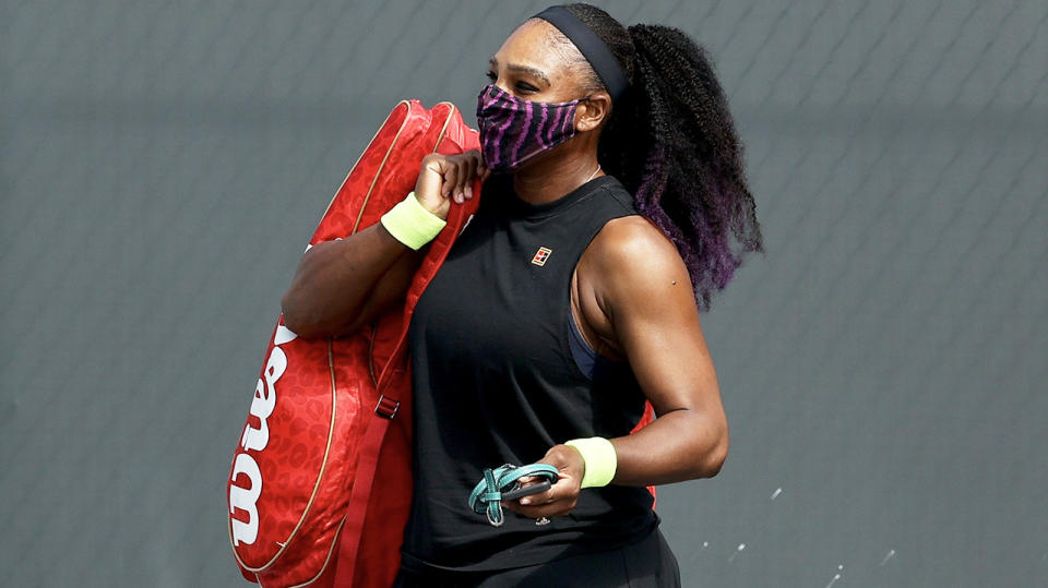 Serena Williams walks across the court with a mask and carrying her bag.