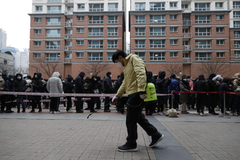 Un funcionario del gobierno rocía desinfectante como medida de precaución contra el COVID-19 cerca de gente que hace fila para comprar mascarilla, en el exterior de una tienda, en Seúl, Corea del Sur, el 28 de febrero de 2020. (AP Foto/Lee Jin-man)