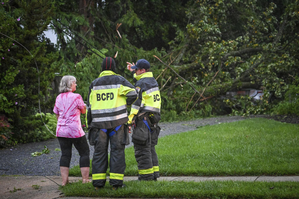 Dale Rogoff Greer, left, talks with Baltimore County firefighters after several trees took out the power lines and fell on her daughter's car by her house on Gittings Avenue in Towson, Md., Monday, Aug. 7, 2023. (Jerry Jackson/The Baltimore Sun via AP)