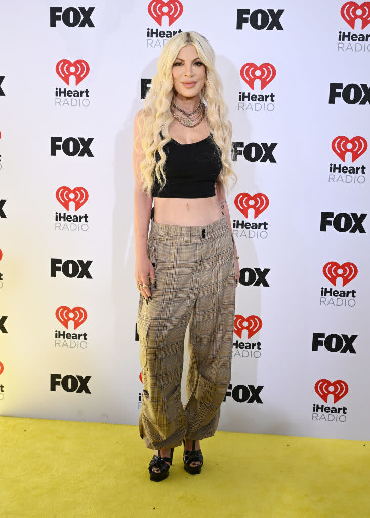 Person on red carpet wearing black top, plaid trousers, and necklaces