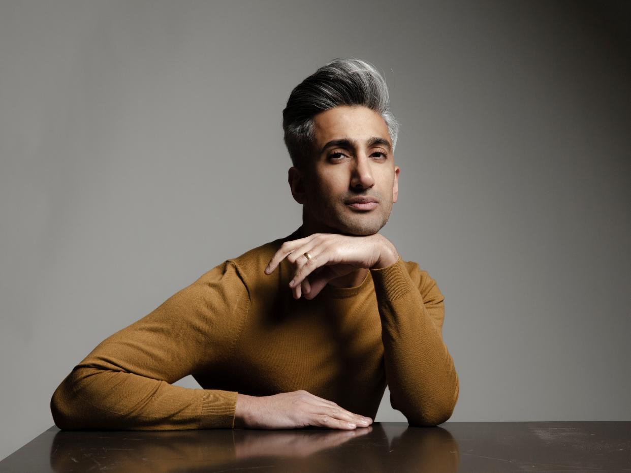 'Queer Eye' TV host Tan France wearing an ochre turtleneck sitting at a black table in front of a gray background.