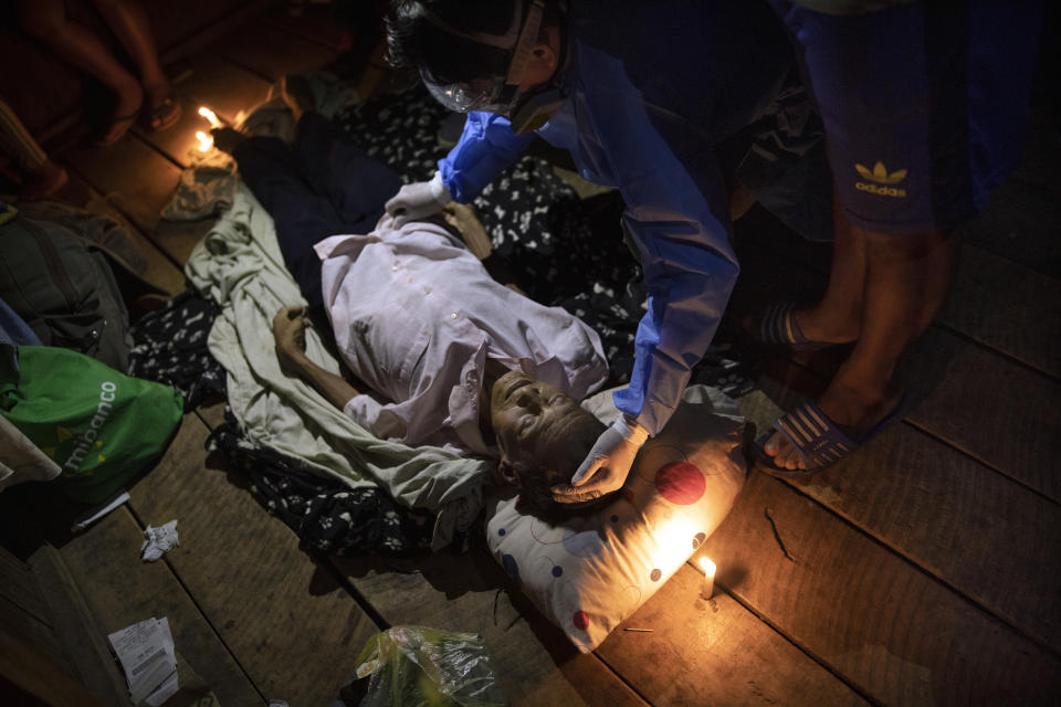 Illuminated with candles and a cell phone blue light, a doctor examines the lifeless body of Jose Barbaran who is believed to have died from complications related to the new coronavirus, in a relative's home in Pucallpa, in Peru's Ucayali region, Tuesday, Sept. 29, 2020. As Peru grapples with one of the world's worst COVID-19 outbreaks, another epidemic is starting to raise alarm: Dengue. (AP Photo/Rodrigo Abd)