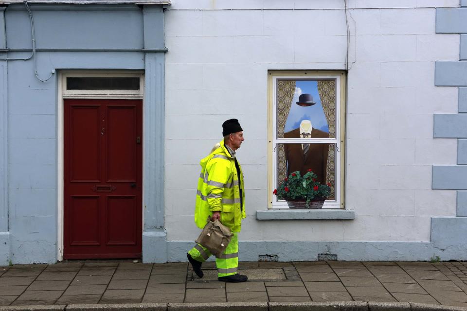 Man walks past an empty building, which has been covered with artwork to make it look more appealing, in the village of Bushmills on the Causeway Coast