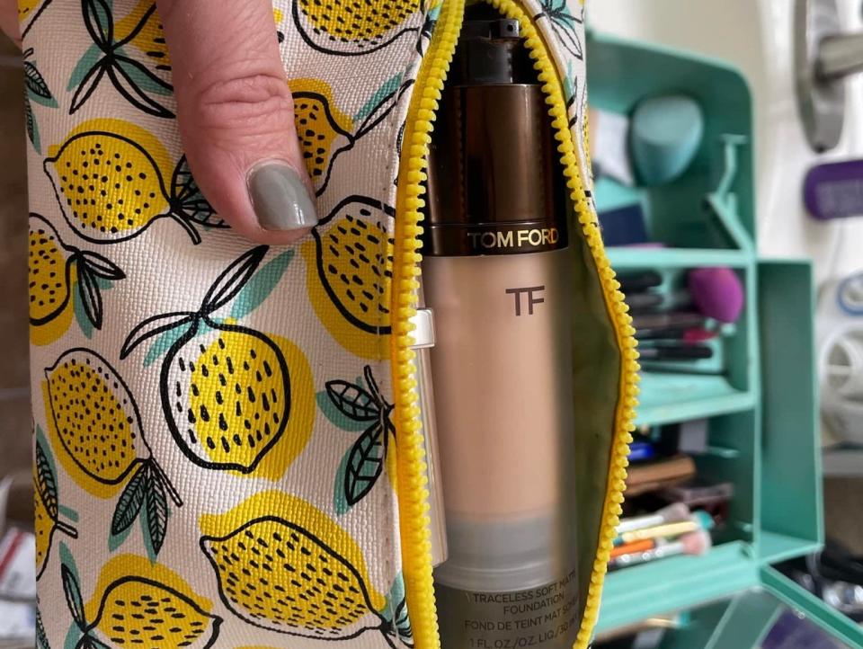 The writer holds the foundation in a makeup bag with illustrations of lemons on it by bathroom sink