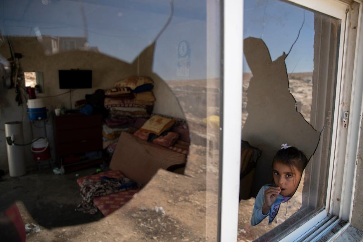 A Palestinian girl looks through her family home's shattered window after a settlers' attack in the West Bank village of al-Mufagara, near Hebron, on Thursday, Sept. 30, 2021. (Nasser Nasser/Associated Press - image credit)