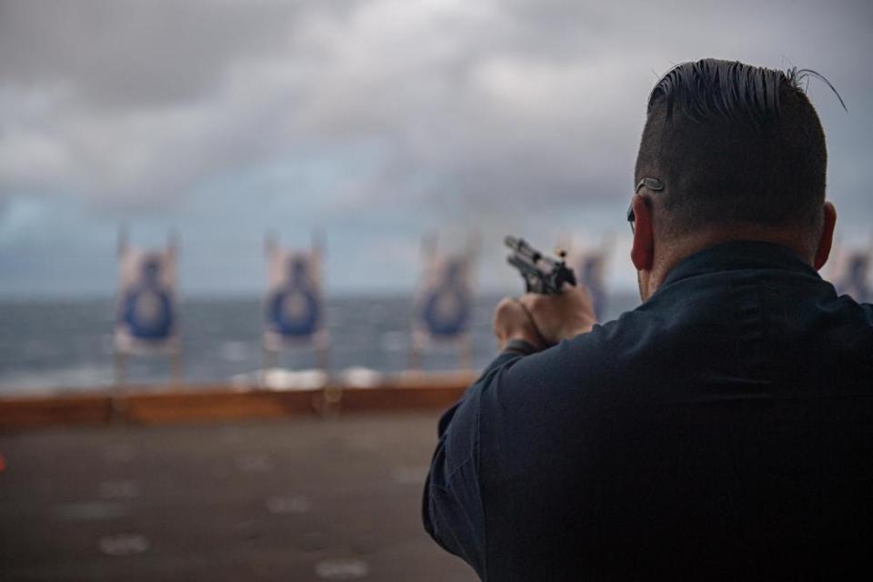 Logistics Specialist 1st Class Steven Lowe, from Mount Holly, assigned to the forward-deployed amphibious assault carrier USS America, fires an M9 pistol during a Navy handgun qualification course while sailing in the Philippine Sea, Jan. 16, 2023.