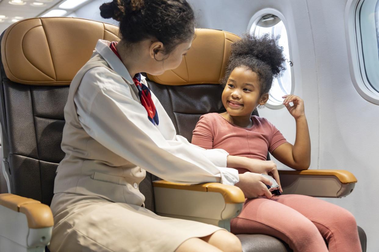 Flight attendant help fasten the seatbelt for young little African American kid after boarding the airplane as a safety procedure before take off
