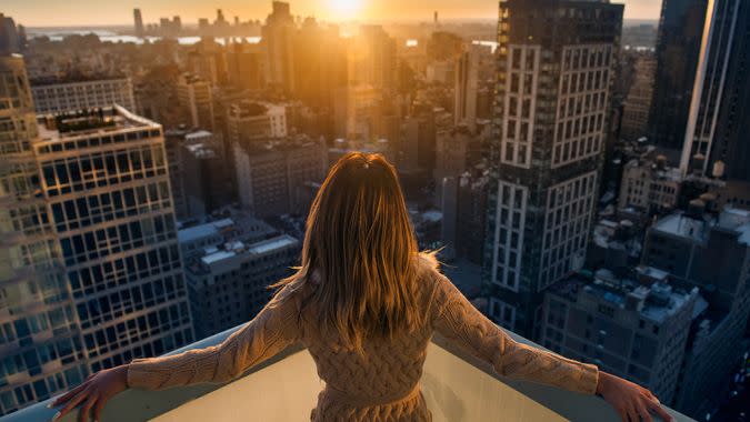 Rich woman enjoying the sunset standing on the balcony at luxury apartments in New York City.