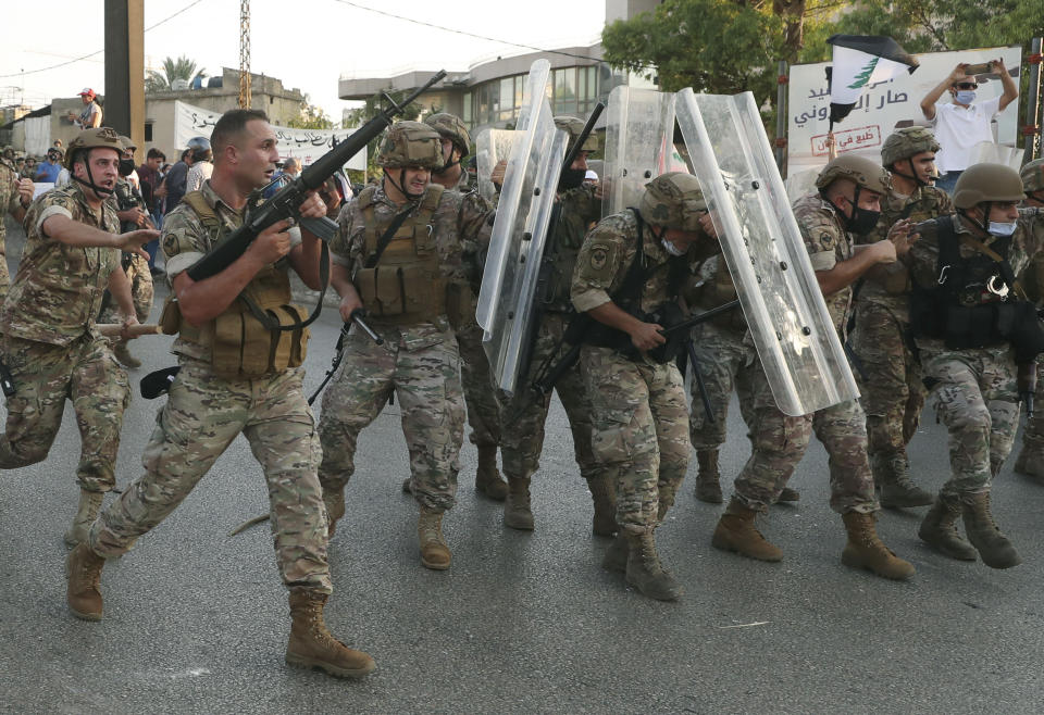 A Lebanese army soldier, left, fires in the air to push back the anti-government protesters as other soldiers protect themselves from the stones, during a protest against the Lebanese President Michel Aoun near the presidential palace, in Baabda east of Beirut, Lebanon, Saturday, Sept. 12, 2020. Soldiers fired rubber bullets and live rounds in the air to disperse hundreds of protesters trying to march to the presidential palace during an anti-government demonstration. (AP Photo/Bilal Hussein)