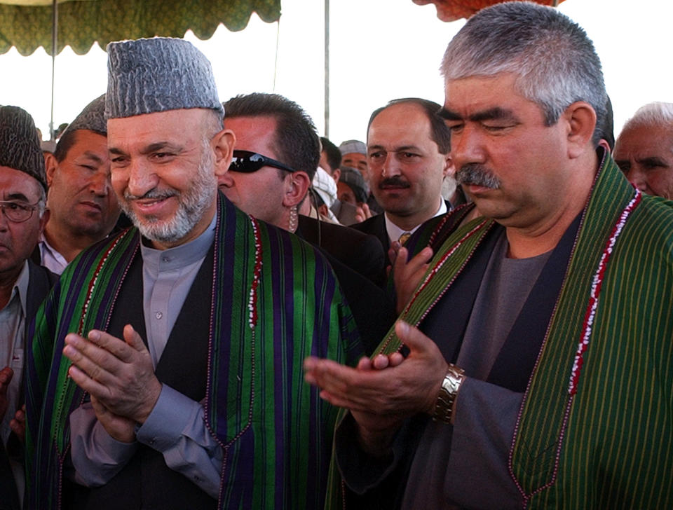 FILE - In this Sunday, Sept. 26, 2004 file photo, Afghan President Hamid Karzai, left, accompanied by the presidential candidate and regional commander General Abdul Rashid Dostum applaud during his visit to Shiberghan, about 400 kilometers (250 miles) northwest of the capital Kabul. Secret contacts are again reported to be underway for an Afghanistan peace deal, but neither analysts nor the belligerents see hope they will succeed. Many wonder whether Karzai even wants a peace deal before the April election. He is ineligible for a third term, and stalling until he is out of office would punt the tough decisions to his successor. And the Taliban still needs to prove it can be trusted not to exact revenge for alleged atrocities by Afghan leaders. The ill-feeling resonates in the case of Rashid Dostum, an Uzbek warlord who the Taliban, as well as Western human rights organizations, accuses of killing thousands of surrendering Taliban during the U.S.-led 2001 invasion. Dostum is running for vice president in the election.(AP Photo/Emilio Morenatti, File)