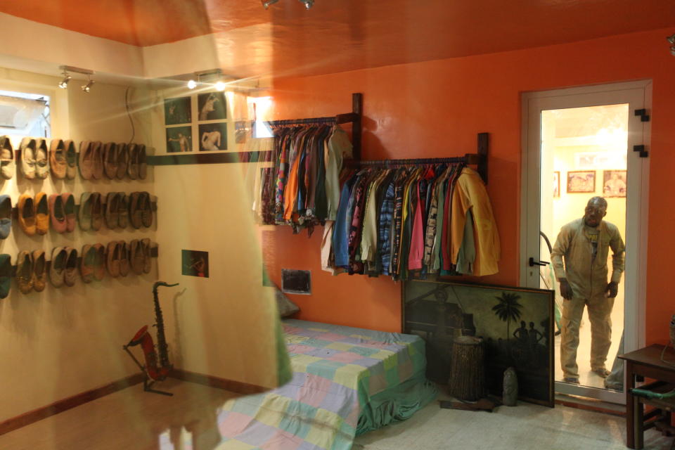 An onlooker peers into the preserved bedroom of singer Fela Anikulapo-Kuti while a reflection of a room containing the musician's shoes and a saxphone can be seen in a reflection in Lagos, Nigeria, on Monday, Oct. 15, 2012. The family of late Afrobeat singer Fela Anikulapo-Kuti celebrated the opening of the Kalakuta Museum on Monday in Lagos in the home the musician once lived in. The opening of the museum comes during Felabration, an annual music festival honoring the singer. (AP Photo/Jon Gambrell)