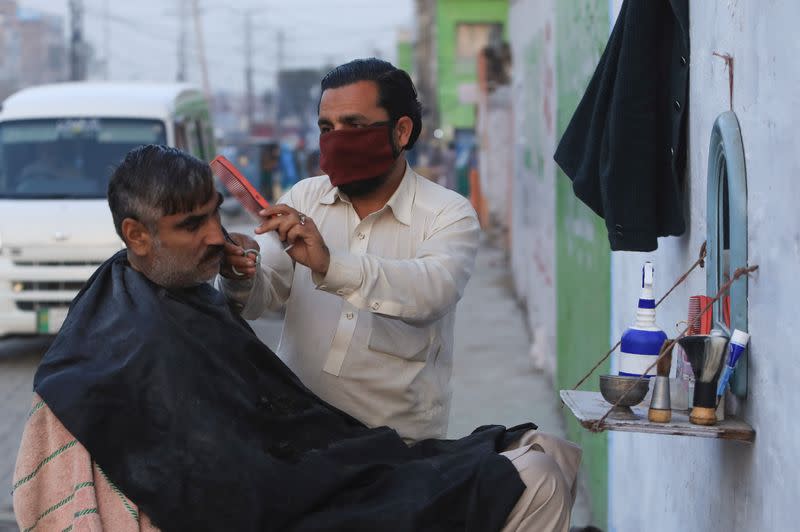 A barber wears a protective mask as a preventive measure amid coronavirus fears, as he gives a haircut to a customer along a road in Peshawar