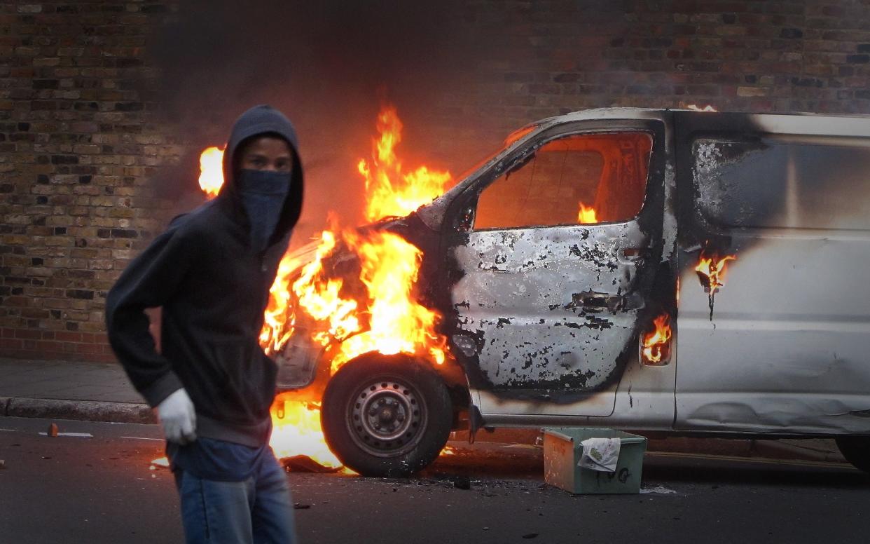 A hooded youth walks past a burning vehicle in Hackney on August 8, 2011 in London - Peter Macdiarmid/Getty Images