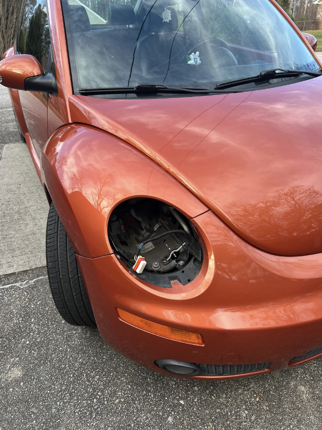 A red car with its front left headlight missing, exposing internal components