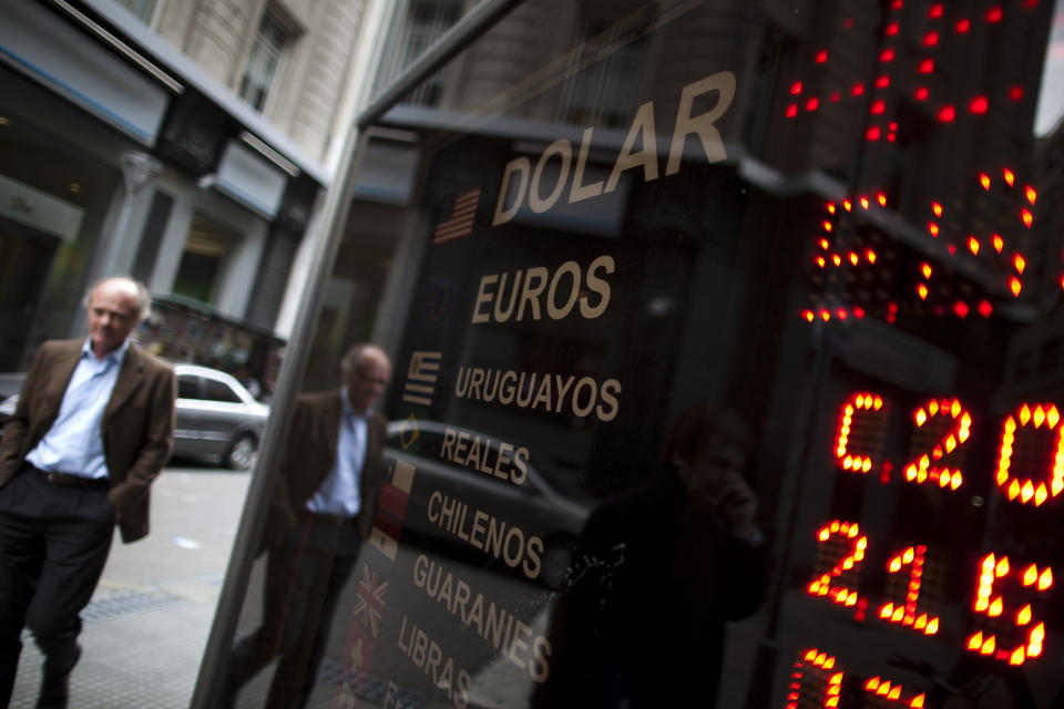 Pedestrians walk past a sign showing the exchange rate for the Argentine peso in Buenos Aires, Argentina, Monday, Sept. 3, 2012. Argentines are increasingly feeling trapped inside their country as currency controls restrict them the foreign cash they need to travel. New rules taking effect this week aim to make using plastic outside the country less affordable by charging 15 percent in taxes on all foreign purchases that appear on credit or debit card bills, plus a 50-percent customs duty on any undeclared goods. (AP Photo/Natacha Pisarenko)