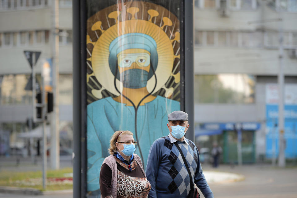 Elderly people wearing masks pass by a depiction of a medical staff wearing protective equipment, executed in the style of Christ Pantocrator, in Bucharest, Romania, Wednesday, April 29, 2020. The artwork, among others depicting medical staff in the manner of religious icons, created by designer Wanda Hutira, is part of a campaign called Thank You Doctors, meant to raise awareness to the work of medical staff fighting the COVID-19 pandemic. Following public pressure by Romania's influential Orthodox church the artworks, described as "blasphemous", will be removed from all locations in the Romanian capital, according to the agency behind the project. (AP Photo/Vadim Ghirda)