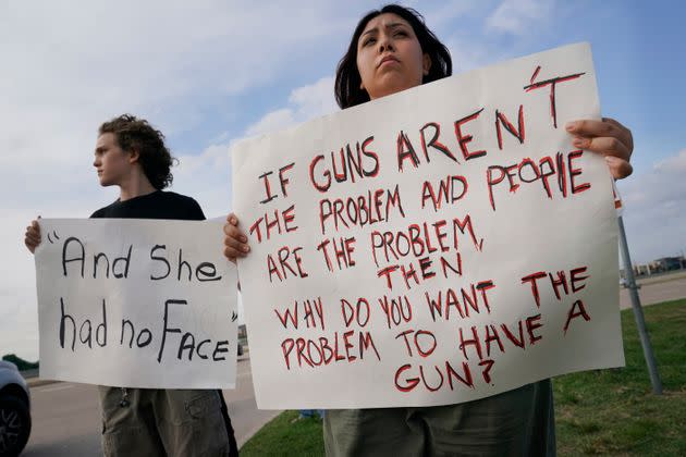 Two teenagers hold protest signs outside a prayer vigil after a mass shooting in Allen, Texas, on May 6. The sign on the left appears to reference a man having said that he found a girl without a face while attempting to aid the shooting victims.