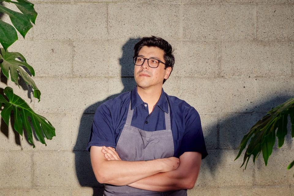 A man in an apron leans against a wall.