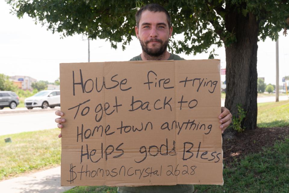 Thomas Shull holds the sign he was using Friday to solicit money from passing motorists at the southwest corner of S.W. Wanamaker and Winding Road.