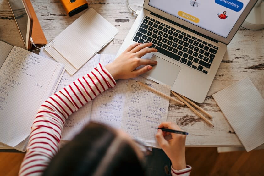 Teenage girl studying online using laptop and writing notes at home during quarantine