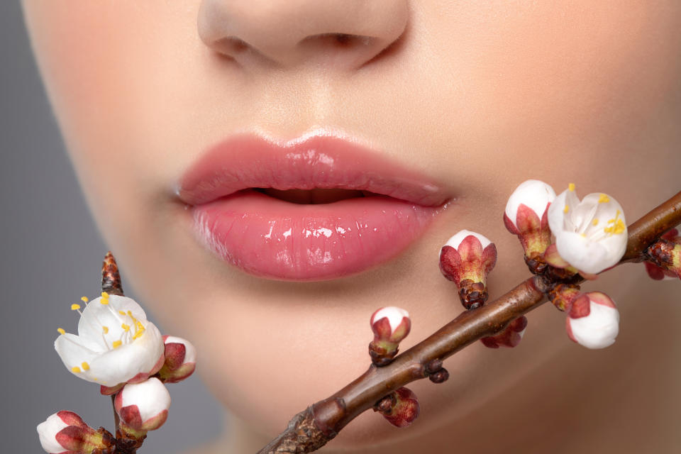 Junges Mädchen mit wunderschönem Nude-Make-up und prallen Lippen. Perfekte natürliche Lippen aus nächster Nähe. In ihrer Nähe sind wunderschön blühende Frühlings-Sakura-Blumen. Professionelle Make-up- und Kosmetologie-Hautpflege.