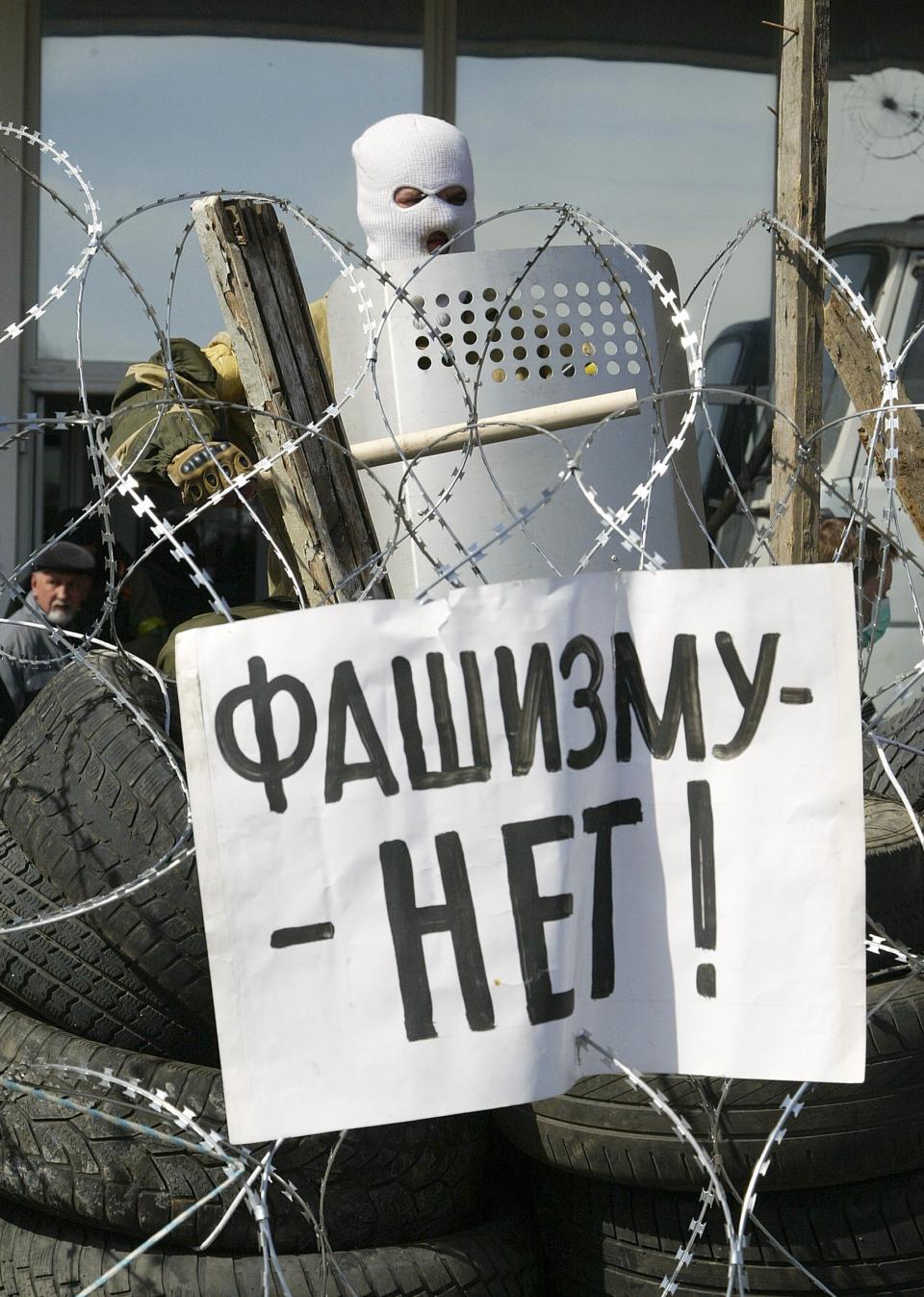 FILE - In this Monday April 7, 2014 file photo a masked man stands atop a barricade with the poster reading "No to fascism!" at the regional administration building in Donetsk, Ukraine. The propaganda assault began during the pro-Western Maidan protests late last year that ousted Ukraine’s pro-Russian president in February: Russian state news media were quick to dismiss the protests as the work of Ukrainian neo-Nazis, a particularly loaded accusation because Ukrainian nationalists collaborating with the Nazis are blamed for horrific reprisal attacks during World War II. (AP Photo/Alexander Ermochenko, file)