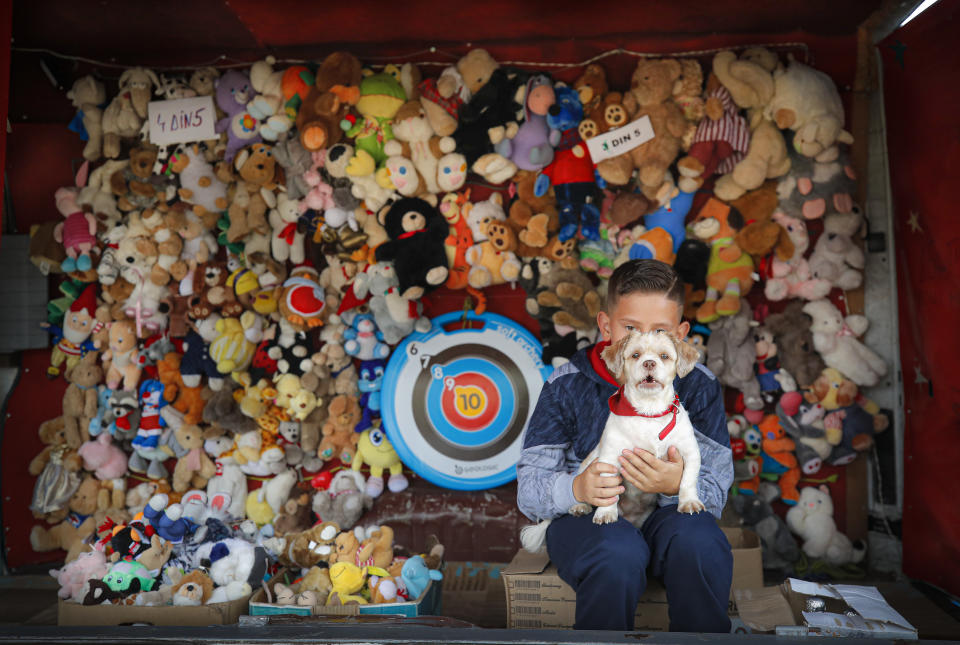 In this picture taken Thursday, Sept. 12, 2019, a child holds Fete, a small dog, at a target shooting stand at an autumn fair in Titu, southern Romania. Romania's autumn fairs are a loud and colorful reminder that summer has come to an end and, for many families in poorer areas of the country, one of the few affordable public entertainment events of the year. (AP Photo/Vadim Ghirda)