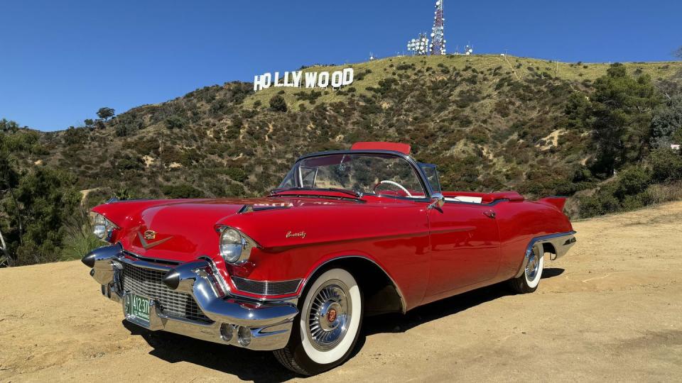 a red car parked on a dirt road with hollywood sign in the background