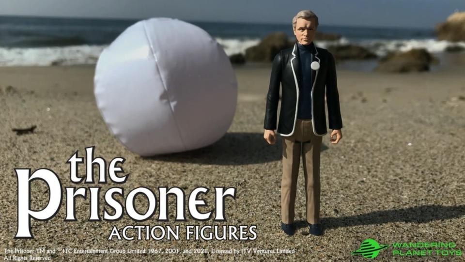 An action figure of The Prisoner's Agent Six on the beach.