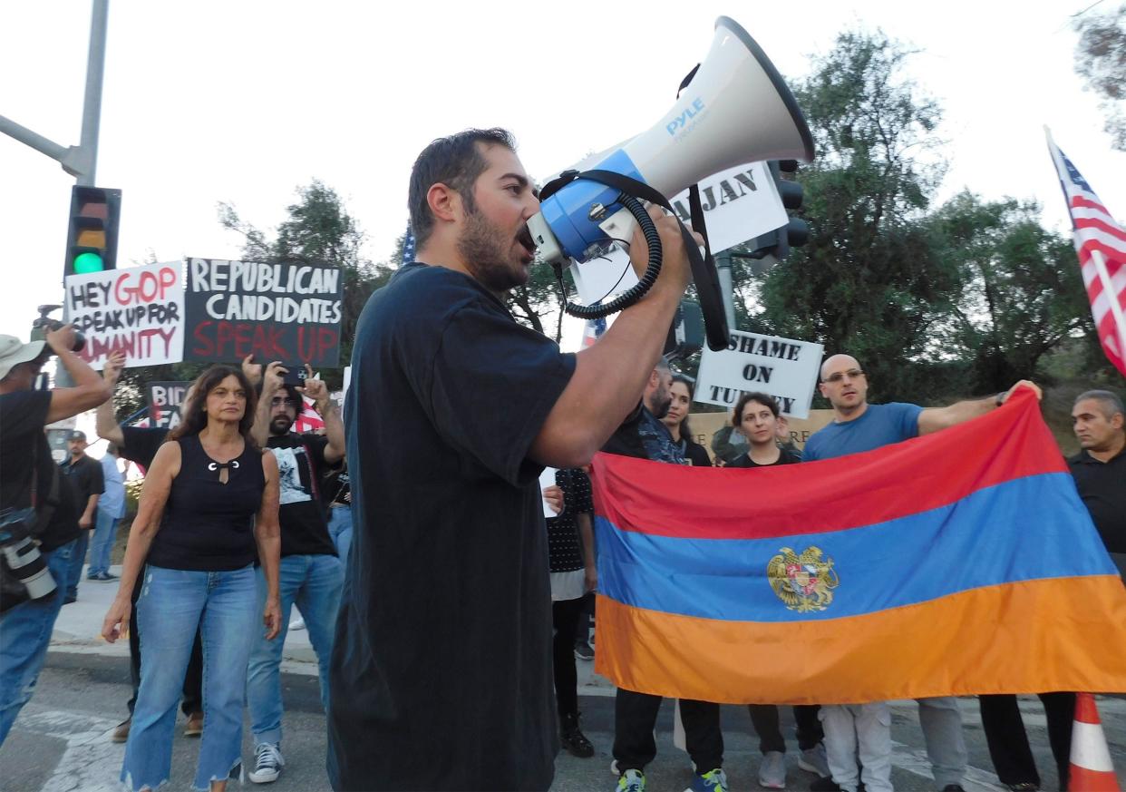 Participants hold signs and the Armenian flag as a man leads chants demanding action against Azerbaijan during a rally Tuesday near the Ronald Reagan Presidential Library & Museum in Simi Valley.