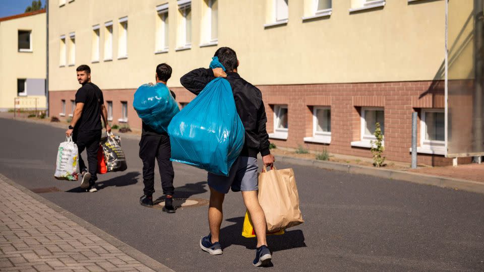 Migrants walk past a housing block at Brandenburg's Central Immigration Authority center, in Eisenhuttenstadt, eastern Germany.  - Odd Andersen/AFP/Getty Images