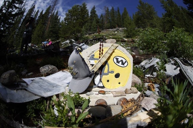 A likeness of the football helmet for the Wichita State Shockers, circa 1970, is draped by a cap as teammates, family members and friends visit the crash site near Loveland Pass on July 27, west of Silver Plume, Colo. Wreckage from the plane, which was one of two being used to take the Shockers to play a football game against Utah State University in Logan, Utah, is still scattered on the mountain top nearly 50 years after the crash close to the Eisenhower Tunnel. [AP Photo/David Zalubowski]