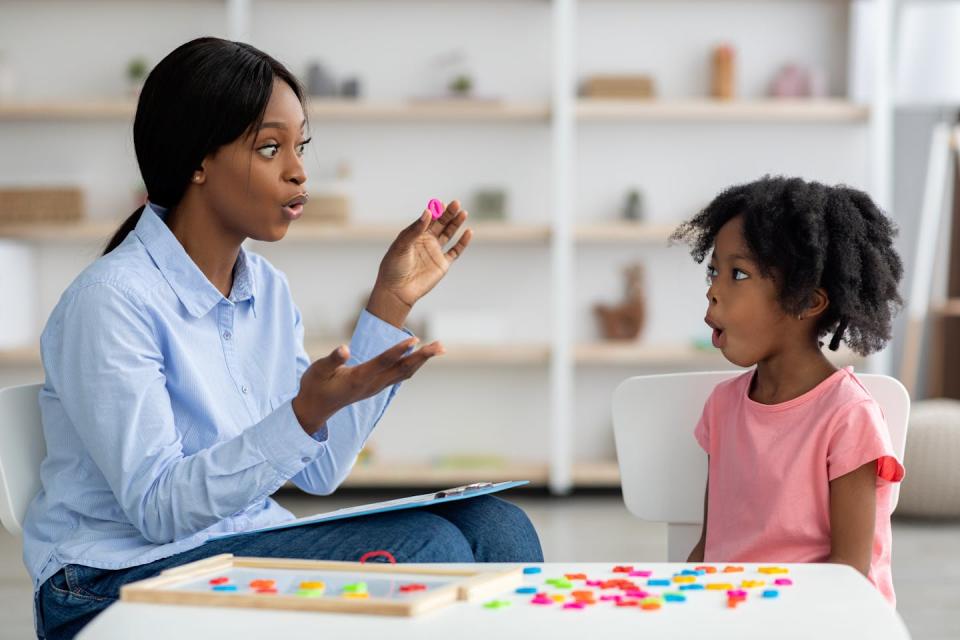 An educator engaging a child at a table while making an expressive face. The child watches closely and mirrors this.