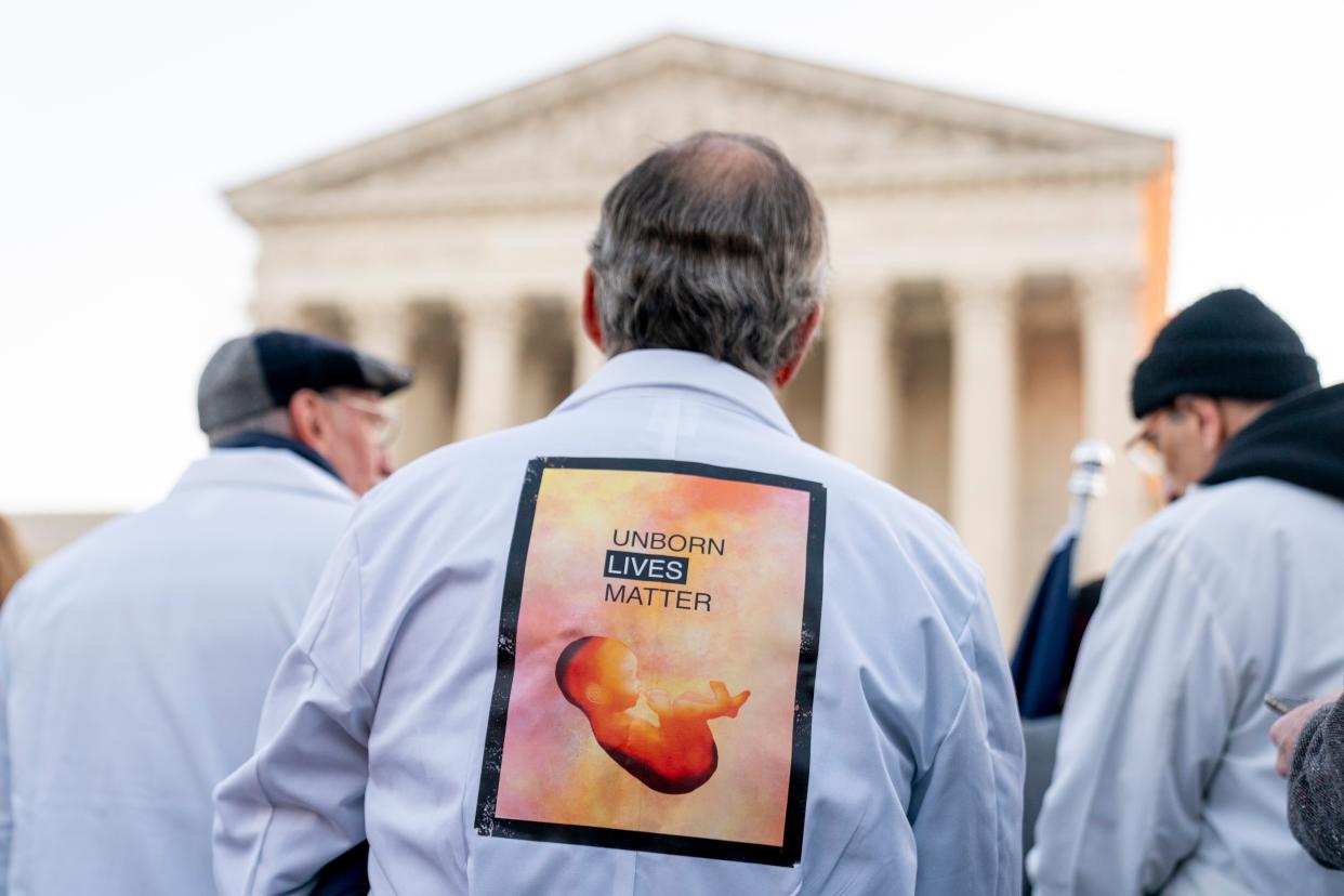 A man wears a sign on his back that reads "Unborn Lives Matter" as he and other anti-abortion protesters wearing doctor's uniforms demonstrate in front of the Supreme Court, Wednesday, Dec. 1, 2021, in Washington, D.C.