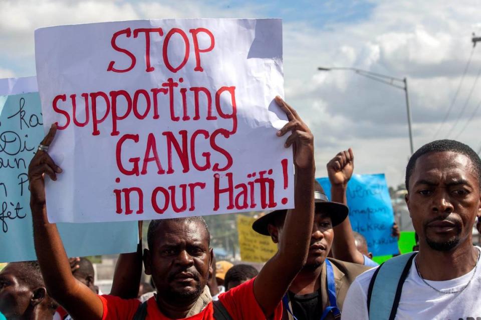 A protester holds up a sign demanding that the support of armed gangs in Haiti cease, in Port-au-Prince, Haiti, Thursday, Dec. 10, 2020.
