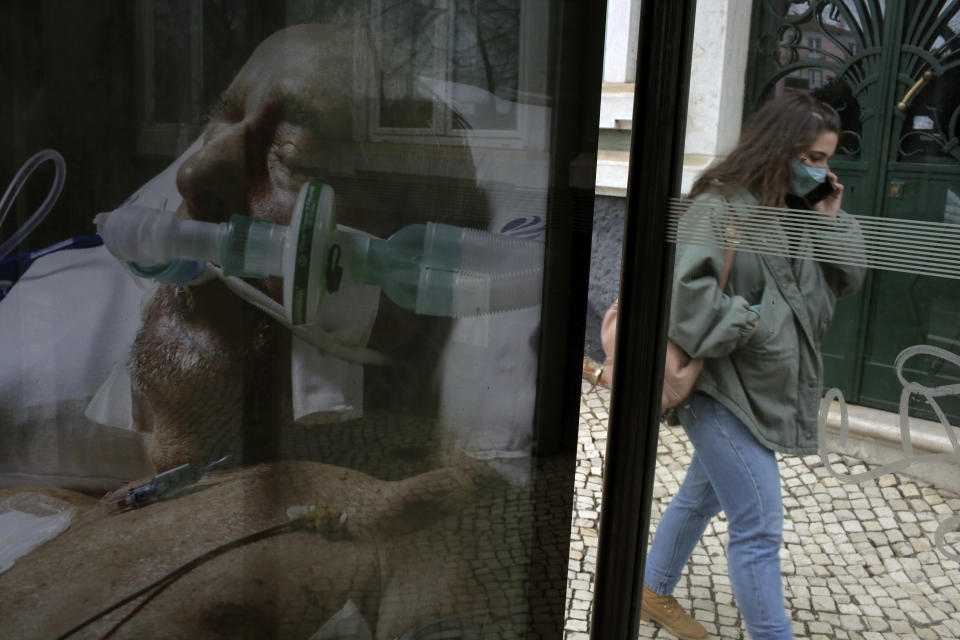 A woman wearing a face mask walks by a poster alerting people to take precautions against the coronavirus, in Lisbon, Wednesday, Jan. 27, 2021. Portugal has had the world's worst rate of new daily COVID-19 cases and deaths per 100,000 population for the past week, according to a tally by Johns Hopkins University. (AP Photo/Armando Franca)