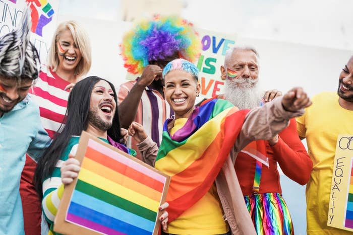 Group of people celebrating LGBT pride, smiling and holding a rainbow flag. Colorful outfits and flags are prominent