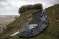 FILE- A damaged inflatable small boat is pictured on the shore in Wimereux, northern France, Thursday, Nov. 25, 2021 in Calais, northern France. The price to cross the English Channel varies according to the network of smugglers, between 3,000 and 7,000 euros. Often, the fee also includes a very short-term tent rental in the windy dunes of northern France and food cooked over fires that sputter in the rain that falls for more than half the month of November in the Calais region. (AP Photo/Michel Spingler, File)