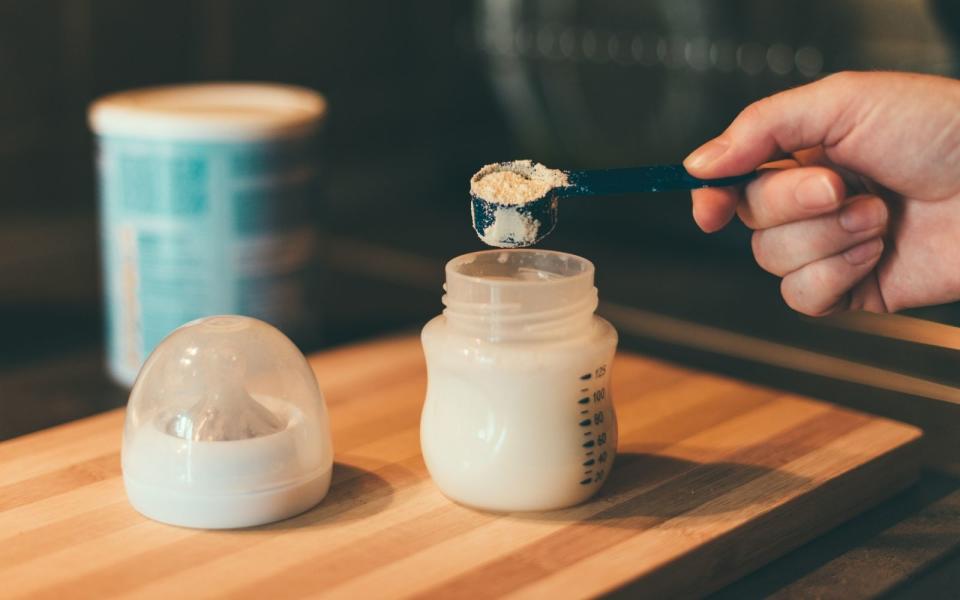 a person pouring a scoop of baby formula into a bottle