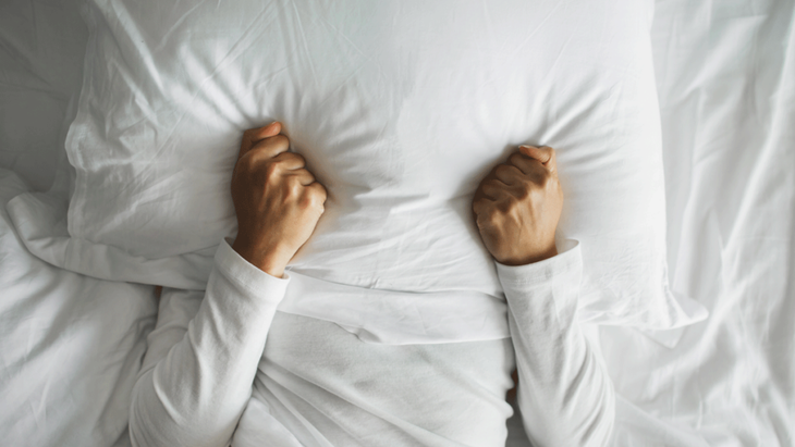 Woman lying in bed with a pillow over her face because she can't sleep