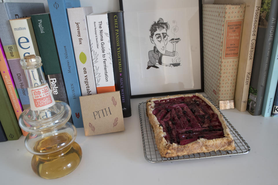 In this May 17, 2019 photo, a rhubarb tart is displayed with a caricature of Jonah Reider and his cookbooks in his New York apartment. In the competitive food world, Reider is a millennial whose cooking is opening doors to adventures far beyond food. (AP Photo/Mary Altaffer)