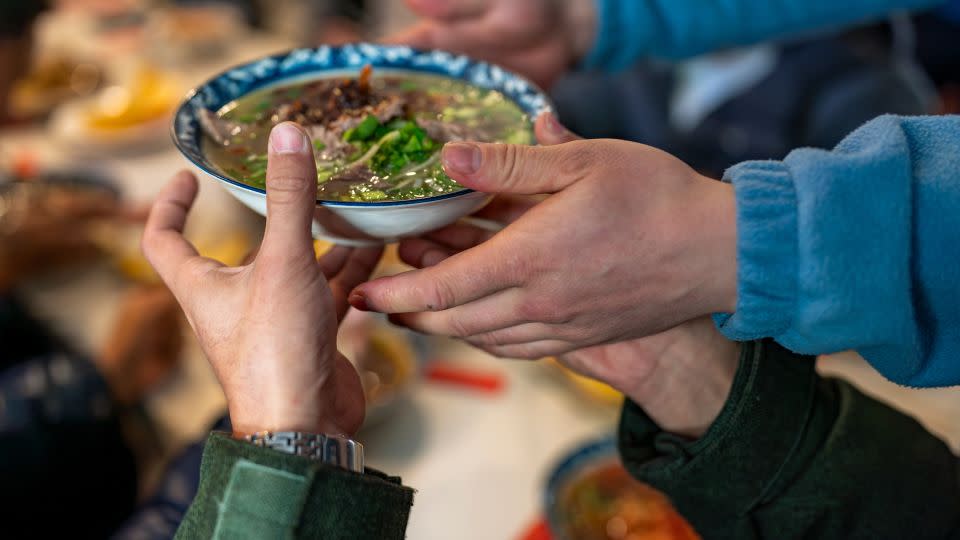 Chinese migrants pass a bowl of soup in a shared apartment for refugees in Flushing, New York. - Evelio Contreras/CNN