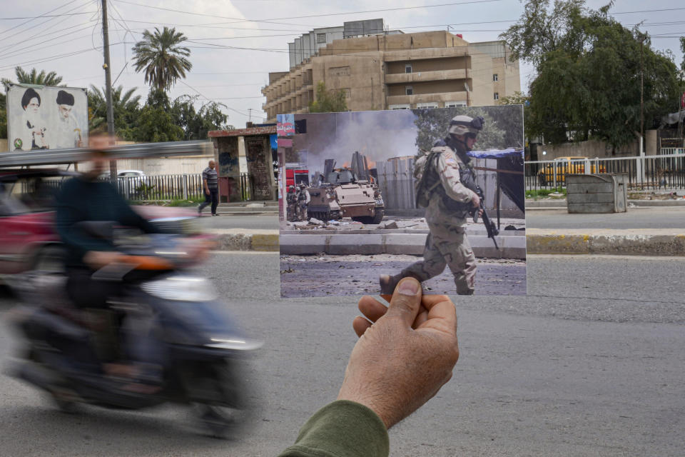 A photograph of car bomb attack on a U.S. military convoy in Baghdad, Iraq, Friday July 15, 2005, is inserted into the scene at the same location Tuesday, March 21, 2023, 20 years after the American led invasion on Iraq and subsequent war. (AP Photo/Hadi Mizban)