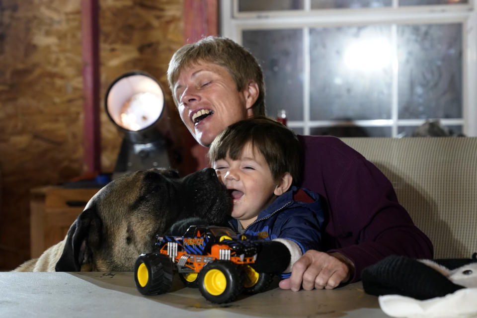 Mary Ann Unson laughs as a family dog licks the face of her great nephew Ricky Trahan III, 1, as one of the family dogs Stella licks his face, on Christmas Eve inside her gutted home, in the aftermath of Hurricane Laura and Hurricane Delta, in Lake Charles, La., Thursday, Dec. 24, 2020. The extended family is living in tents and campers on the property, having all lost their homes to the storms. (AP Photo/Gerald Herbert)